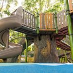 beige spiral slide coming off a deck being supported by a tree trunk climber