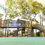 playground equipment with accessible ramps and customised log tunnel slide with trees in the background