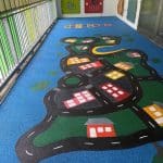 Blue rubber wetpour surfacing with a painted on toy car track graphic with multi coloured houses and trees