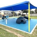 Bright blue shade structure with yellow support posts over children's play area