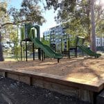 Children's playground with 2 green slides and bark mulch surfacing