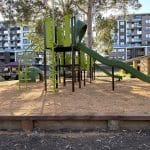 Children's playground with a green wavy slide and bark mulch surfacing