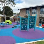 Climbing wall with honeycomb style panelling in a turquoise blue colour and sky blue support posts with purple and blue rubber surfacing