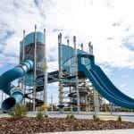 Two tall cylindrical towers each with a lagoon colour slide with a perferated black bridge connecting the two towers