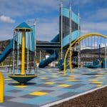 Modern outdoor playground featuring colourful climbing structures, slides, and interactive equipment set against a scenic hillside backdrop