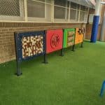 Four multi coloured play panels installed on Navy Blue posts in tandem in a synthetic grass surface.