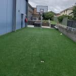 A green synthetic grass surfaced area with a basketball tower and backboard.