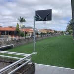 A green synthetic grass surfaced area with a basketball tower and backboard.