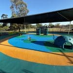 Large open rubber wetpour area with free standing individual play items under a shade structure