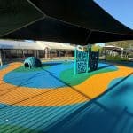 Large open rubber wetpour area with free standing individual play items under a shade structure