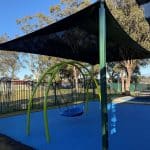 Arched bright green framed swing with large plastic bucket style seat underneath a large shade structure