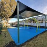 Arched bright green framed swing with large plastic bucket style seat underneath a large shade structure