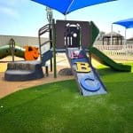 Colorful children's playground featuring an alphabet-themed climber, inclusive climbing structure, and soft rubber safety surfacing—promoting early learning and active play in a shaded, family-friendly outdoor environment.