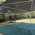 Inground sandpit with green sandpit cover made from mesh material underneath a steel framed shade structure with charcoal shade cloth material