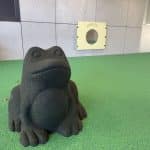 A playful frog sculpture set on green rubber soft‑fall surfacing beside a wall‑mounted circular mirror panel. This interactive area supports sensory exploration and imaginative play, ideal for early learning centres, schools, and sheltered outdoor play spaces.