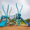 playground with double light blue slide and tall bendy posts in different shades of blue and green