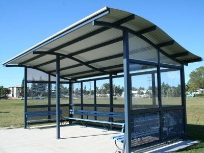 Bus stop shelter with large wave roof design with seating and clear windows