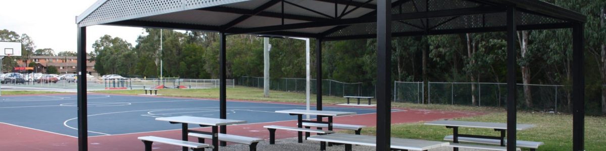 Peaked roof shelter over table and bench seating next to basketball court
